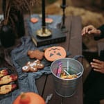 a person sitting at a table with halloween decorations and a bucket of candies