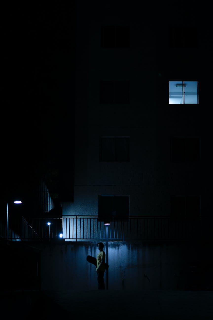 boy with skateboard standing in front of building at night